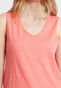 Top sin mangas color coral con diseño de escote en forma de V, hecho de una tela suave y ligera con un acabado ligeramente texturizado.