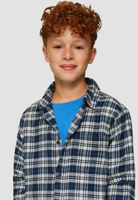 Geruite flanelhemd in blauw en wit, met een button-down kraag en borstzak, gedragen over een blauw crewneck t-shirt.