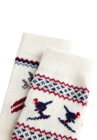 Bijele pletene čarape s crvenim i mornarskim uzorcima, s motivima skijaša i geometrijskim dizajnom blizu rubova.