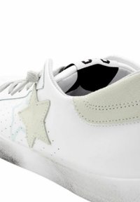 Sneaker bianco con pelle perforata, stella in suede grigio, lacci piatti e suola in gomma texturizzata. Design minimalista e finitura liscia.