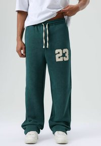 Groene fleece joggingbroek met een ontspannen pasvorm, voorzien van een grote witte "23" tekst op het linkerbeen en een verstelbare tailleband met trekkoord.
