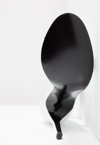 Chaussure à talon haut blanche avec un bout pointu, un dessus en cuir lisse et une semelle noire texturée. Le talon est fin et effilé. Design minimaliste.