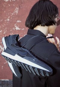 Černé tenisky Nike s kombinací texturovaných materiálů, včetně semiše a síťoviny, mají bílou mezipodešev a odolnou černou gumovou podrážku.