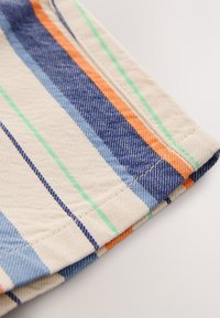 Beige fabric with green, blue, and orange vertical stripes and detailed stitching on a folded edge.