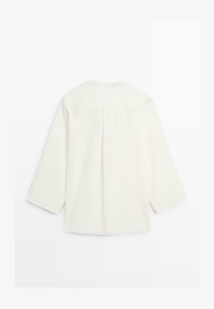 Langærmet hvid skjorte med rygstykke og middelstykke, vist fladt med bagsiden opad på en hvid baggrund.