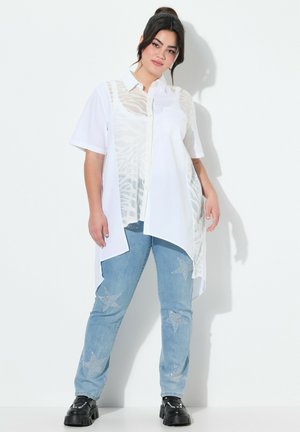 Chemise blanche à manches courtes avec un panneau transparent texturé, associée à un jean bleu clair avec des embellissements en forme d'étoile argentée. Chaussures à plateforme noires.