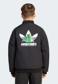 Svart sweatshirts med gröna accenter, med en pixelerad Minecraft-design på baksidan som föreställer en creeper och zombier. Texten lyder "MINECRAFT."