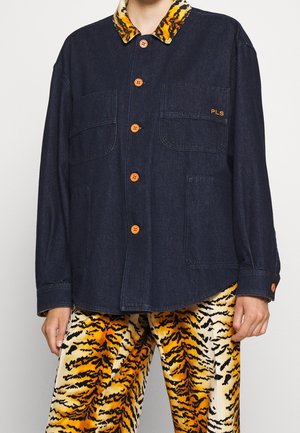 Dark denim jacket with orange buttons and tiger-print collar, worn with matching tiger-striped pants on a standing person.