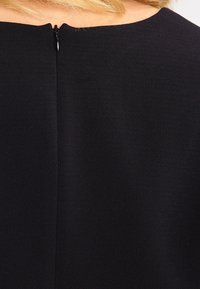 Abito nero con una texture liscia, caratterizzato da una cerniera nascosta sul retro e un collo rotondo, che enfatizza un design minimalista.