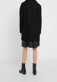 Svart ullkappa med rak passform och slagkrage, med en minimalisitisk design. Matchad med en svart läderkjol och ankelstövlar.