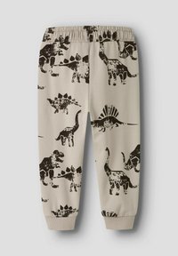 Pantalones de chándal beige con patrones de dinosaurios negros, con una cintura elástica y puños en los tobillos. Textura de tela suave, diseño casual.