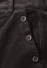 Tessuto di velluto a coste nero con righe verticali, caratterizzato da quattro bottoni metallici su un flap diagonale, che aggiungono dettaglio al design.