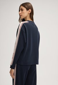 Donkerblauwe sweatshirt met witte en bordeauxrood gestreepte mouwen, met een losse pasvorm en een klassiek rond decolleté ontwerp.