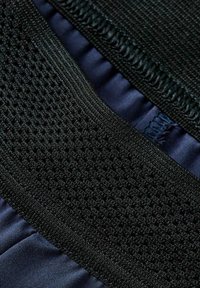 Nahaufnahme von schwarzem Mesh-Stoff mit strukturiertem gewebtem Muster und glattem, dunkelblauem Stoff darunter.