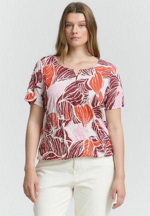 T-shirt à manches courtes avec un décolleté arrondi, présentant un motif de feuilles rouges et orange sur un fond rose pâle. Tissu léger et texturé.