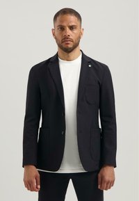 Blazer negru din material, cu rever în formă de notch, două buzunare frontale și închidere cu un singur buton. Purtați peste un tricou alb.