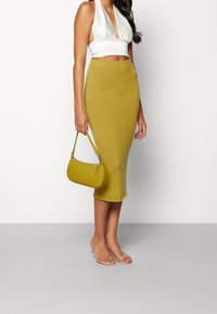 Bílý saténový halter top, žlutá žebrovaná midi sukně a texturovaná žlutá kabelka se stříbrným páskem. Průhledné ploché sandály.