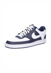 Sneakers Nike con una parte superiore in pelle bianca e accenti blu navy, perforazioni sulla punta e una suola in gomma bianca. I lacci bianchi completano il design.