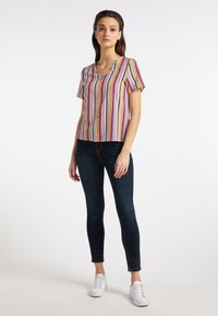 Multifarvet stribet bluse med korte ærmer, V-hals og knapdetalje, parret med mørke skinny jeans og hvide sneakers. Glat tekstur.