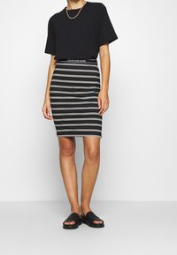 Svart t-shirt kombinerad med en svart och vit randig pennkjol. Outfiten har en märkesmidja och platta, svarta sandaler.