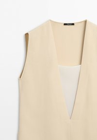 Sleeveless beige vest with deep V-neck and visible inner lighter beige layer, displayed on a white background.