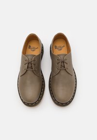 Paire de chaussures en cuir taupe Dr. Martens avec des lacets marron, une surpiqûre jaune autour des semelles noires, vue de dessus sur fond blanc.