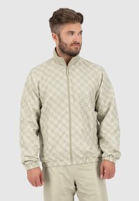 Helles beiges Zip-Jackett mit einem Diamantmuster, elastischen Bündchen und einem elastischen Saum. Aus glattem, strukturiertem Stoff gefertigt, eignet sich für die Freizeit.