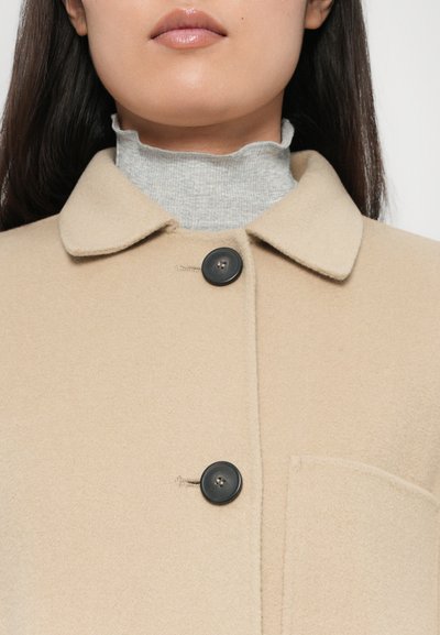 Beige wool coat with a collared neckline, featuring two black buttons and a side pocket, layered over a gray ribbed turtleneck.