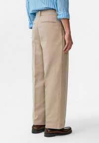 Beige wijde broek gemaakt van stevig materiaal, met een enkele achterzak, een op maat gemaakte tailleband en een gladde textuur.