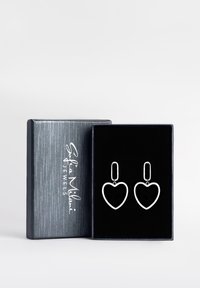 Silverfärgade hjärtformade örhängen med öppna ramar, hängande från en rektangulär post. Visas i en presentbox klädd med svart sammet.