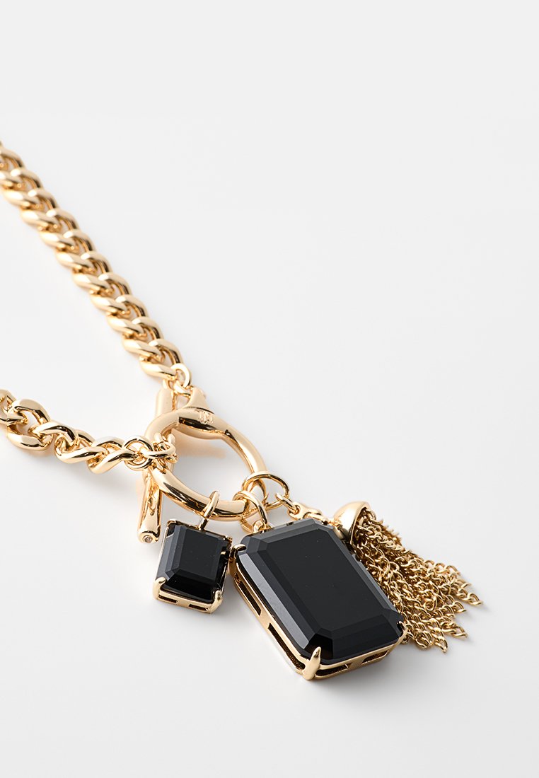 Złoty naszyjnik z łańcuchem, zawierający dwa czarne, kanciaste kamienie i frędzel, podkreślający metalowe akcenty oraz błyszczące wykończenie.