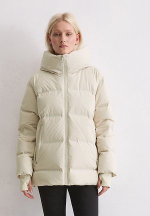 Giacca puffer beige chiaro con collo alto, chiusura con zip e tasche laterali. Il tessuto appare liscio con una texture trapuntata.