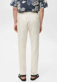 Crèmekleurige linnen pantalon met een rechte snit, voorzien van achterzakken en vergulde knopen, gecombineerd met zwarte sandaal.