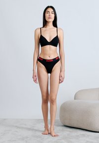 Czarny zestaw bielizny składający się z biustonosza z głębokim dekoltem i majtek z wysokim stanem. Charakterystyczna czerwona gumka z napisem "HUGO". Gładka faktura, minimalistyczny design.