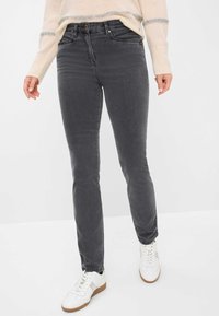 Jeans attillati grigi con una texture liscia, sbiadimenti sottili e design classico a cinque tasche, abbinati a sneakers bianche.