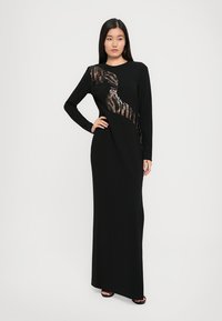 Zwarte jurk met lange mouwen, voorzien van een zijaccent van paillettenstof in een slanke ontwerp. Gladde textuur met een aansluitende silhouet.