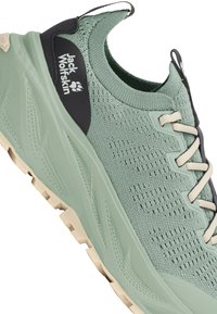 Chaussure de sport Jack Wolfskin vert clair avec dessus en maille, semelle épaisse, lacets beige et écusson logo noir sur le côté.