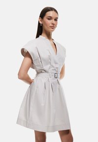 Hellgraues Kleid mit kurzen, weiten Ärmeln, V-Ausschnitt, Gürtel in der Taille und plissiertem Rock. Glattes Gewebe mit minimaler Textur.