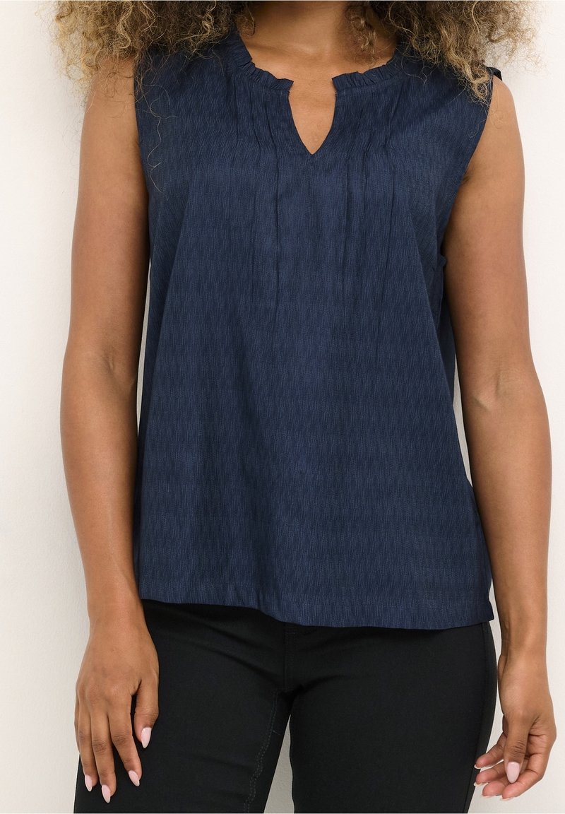 Mörkblå ärmlös blus med en subtil randig textur, V-ringning och rynkdetaljer vid axlarna. Slät tygyta.