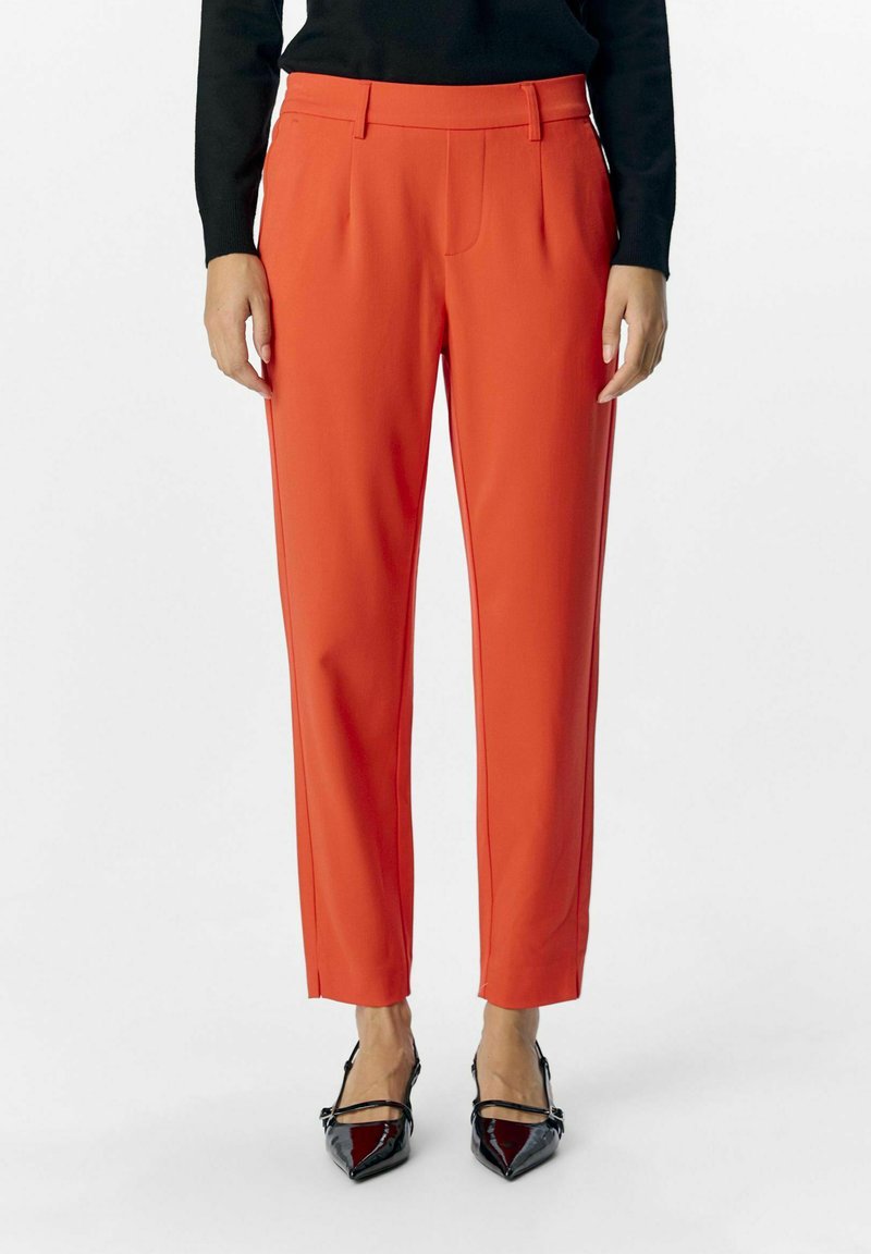Pantalons rouges sur mesure en tissu lisse avec une taille mi-haute, des poches latérales et des jambes légèrement effilées. Assortis avec des talons noirs pointus.