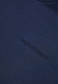 Sudadera azul marino oscura hecha de una tela suave, con un sutil logo bordado de "Peak Performance" en la parte frontal.