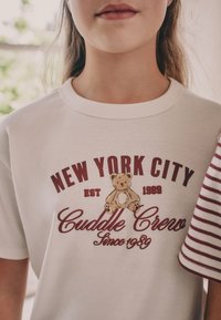 Hvid bomuld T-shirt med bordeauxrød grafisk tekst "NEW YORK CITY" og en bjørneillustration, med rund hals og korte ærmer.