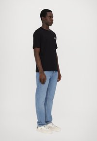 Svart bomulls t-skjorte med korte ermer, som har en liten hvit logo på brystet, kombinert med lyseblå straight-leg jeans og hvite joggesko.