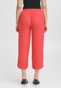Leichte, korallenfarbene weit geschnittene Hose mit elastischem Bund. Weiche Textur und kurze Länge, die direkt über den Knöcheln endet.