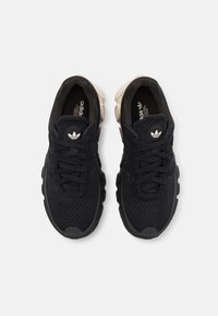 Chaussures de sport noires avec tige en mesh et daim, bout rond, lacets, semelle rembourrée, et logo iconique à trois bandes sur la languette.