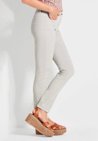 Helle graue Skinny-Jeans mit glatter Textur, kombiniert mit braunen Plattform-Sandalen, die überkreuzte Riemen und geflochtene Keil-Details haben.