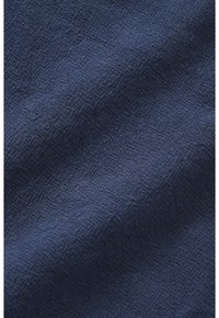 Donkerblauwe stof met een subtiel gestructureerd rasterpatroon en zichtbare geweven vezels die zachte plooien en schaduwen creëren.