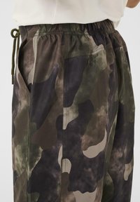 Camo zīmējuma bikses ar elastīgu jostu un diegu valkātas ar gaiši krāsotu topu, kas ir īss līdz jostai.