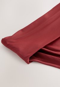 Gros plan d'un tissu rouge plié montrant une texture lisse et des coutures soignées sur une manche de vêtement ou une jambe de pantalon.
