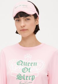 Máscara de sono rosa com "Rainha do Sono" em texto verde. Tecido suave com uma textura lisa. Apresenta um formato contornado para conforto.